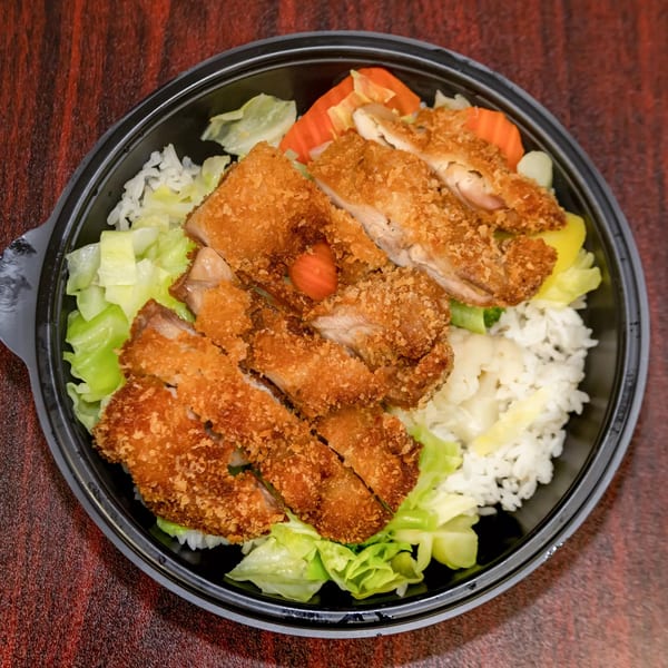 F's Hawaiian Food's chicken katsu plate with rice, cabbage, and pickled vegetables in a black bowl.
