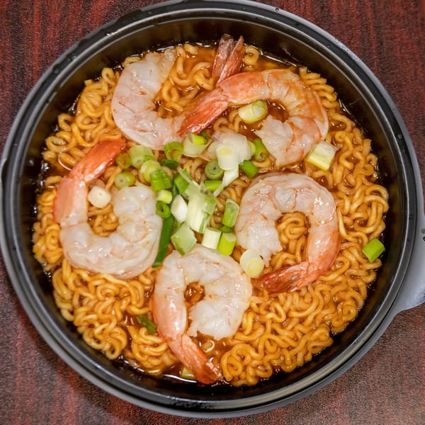 Hawaiian shrimp ramen with green onions in a black bowl on a wooden table.