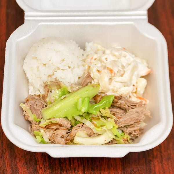 Hawaiian plate lunch with kalua pig, cabbage, rice, and macaroni salad in a white takeout container.
