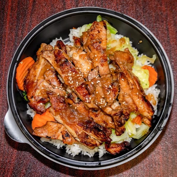 F's Hawaiian Food's grilled chicken with sesame seeds, rice, cabbage, and carrots in a black bowl.