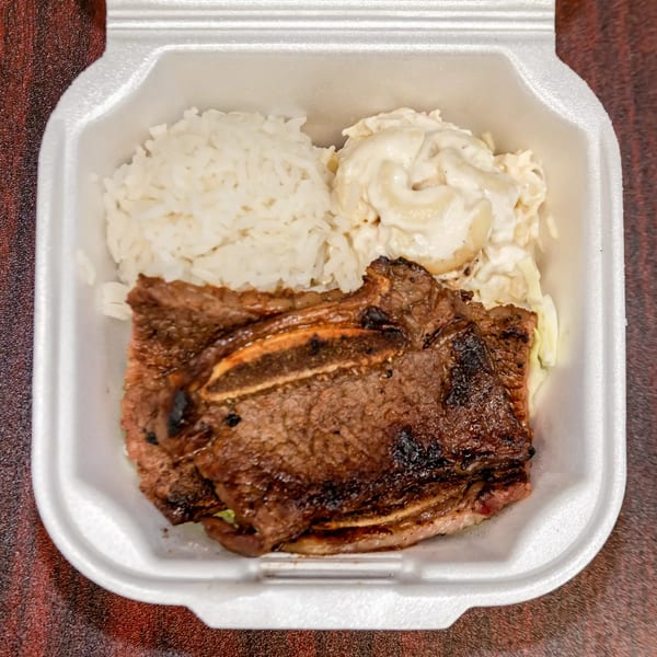 F's Hawaiian Food kalbi short ribs, white rice, and macaroni salad in a white takeout container.